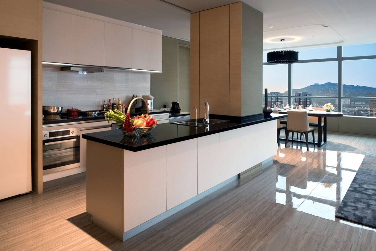 A modern kitchen with a central island, built-in oven, and a dining area with a view.