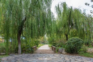 Un sendero de piedra que atraviesa un jardín con sauces llorones y un puente de madera.