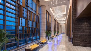 A spacious lobby with large windows, a long reception desk, and a row of white tables and chairs. - Hilton Jinan South Hotel & Residences (Jinan)