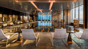A modern hotel lobby with a spacious seating area, a reception desk, and large windows offering a city view. - Hilton Jinan South Hotel & Residences (Jinan)