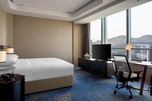 A hotel room with a bed, a desk with a chair, a television, and a large window offering a city view. - Hilton Jinan South Hotel & Residences (Jinan)