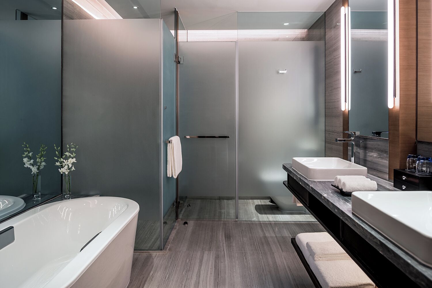 A modern bathroom with a glass shower enclosure, two sinks, and a large bathtub.