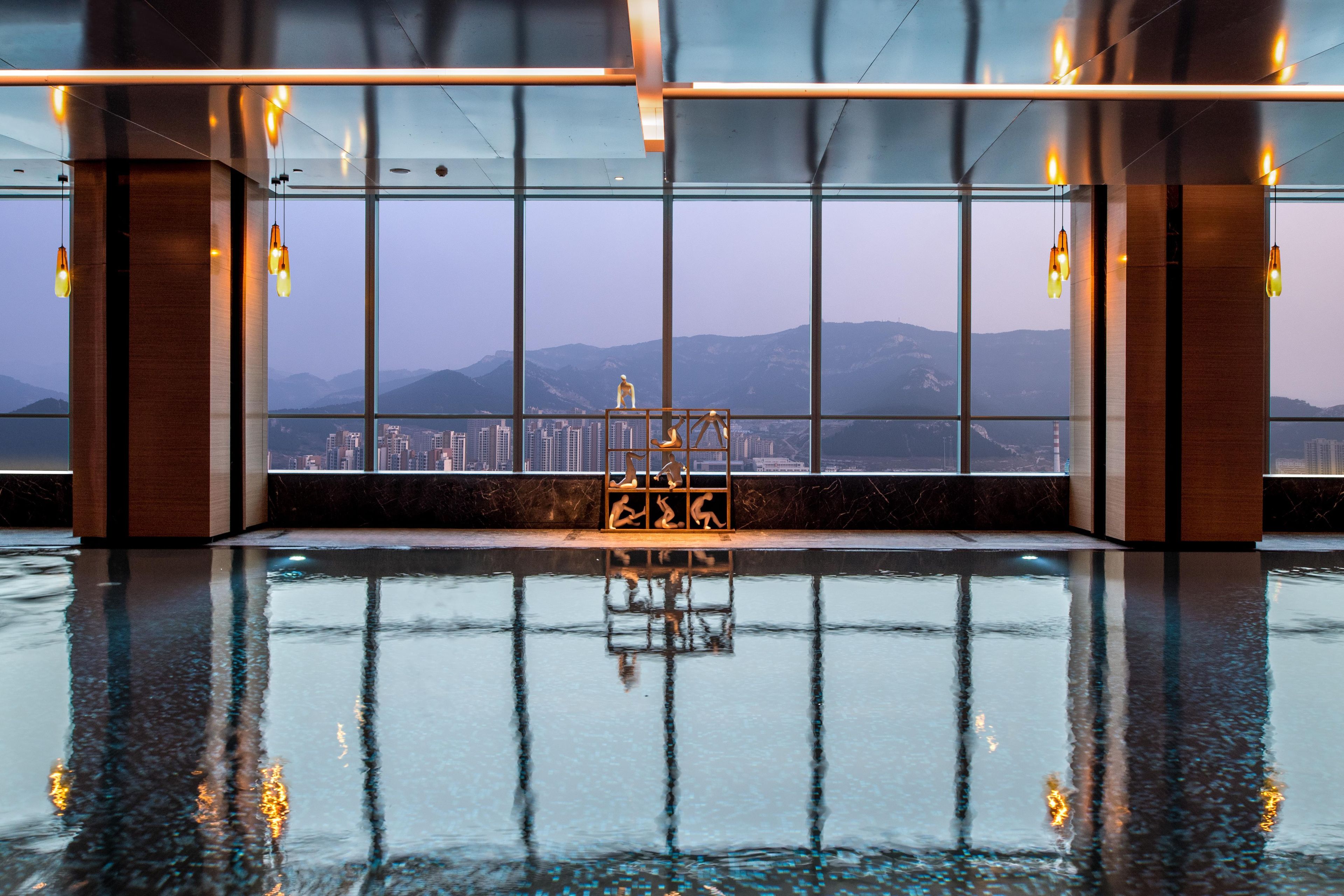 A modern indoor pool with a clear view of a cityscape and mountains in the background.