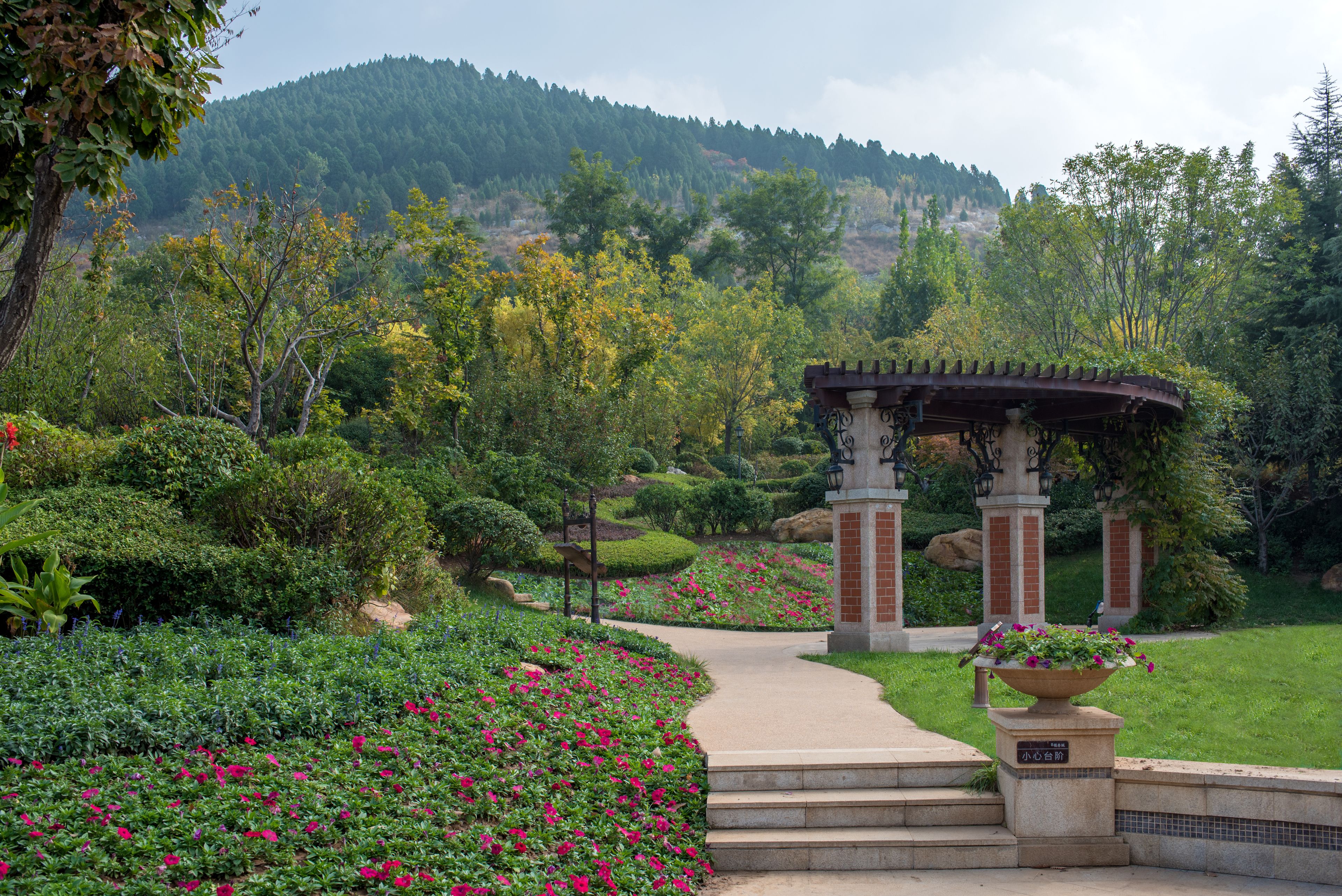 A garden pathway leading to a gazebo with a stone base and a flower pot.