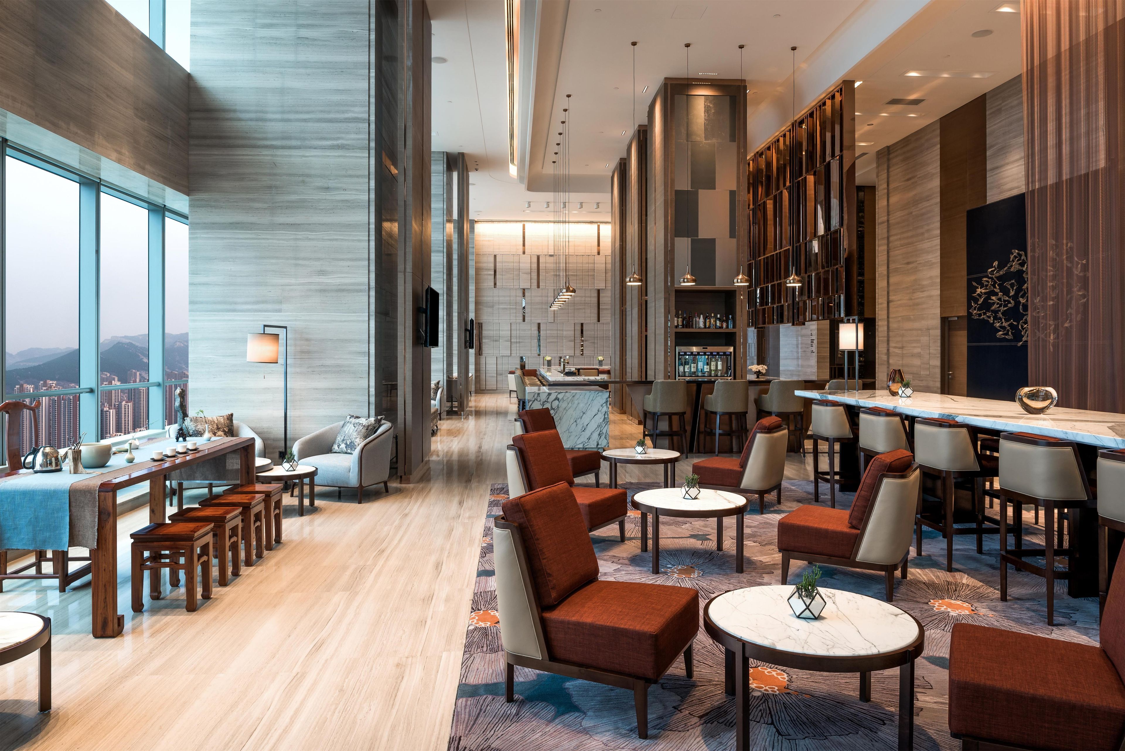 Un hall d’hôtel moderne avec un bar, des espaces pour s’asseoir et une vue sur la ville.