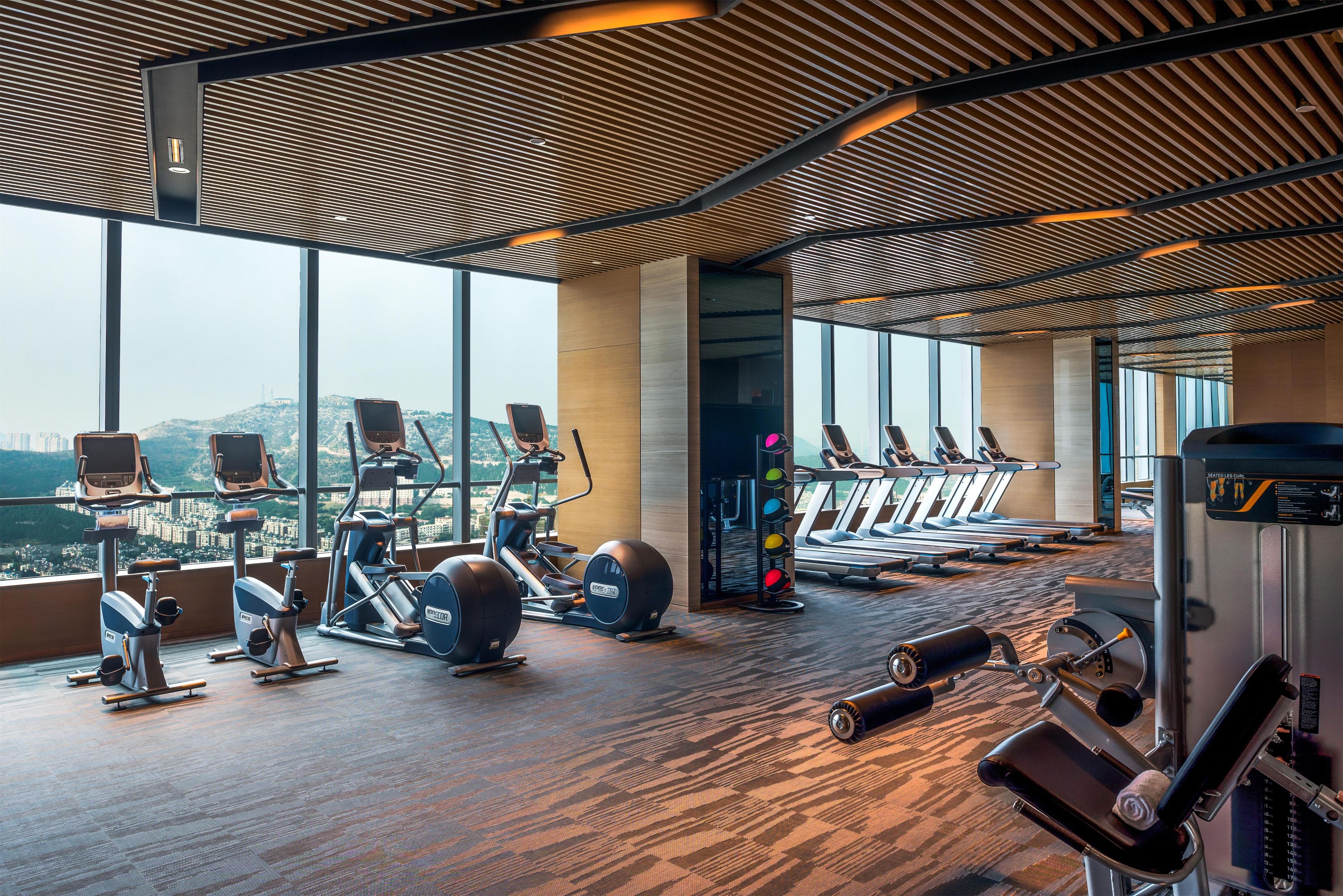 Una palestra con attrezzature per esercizi, ampie finestre e vista sulla città.