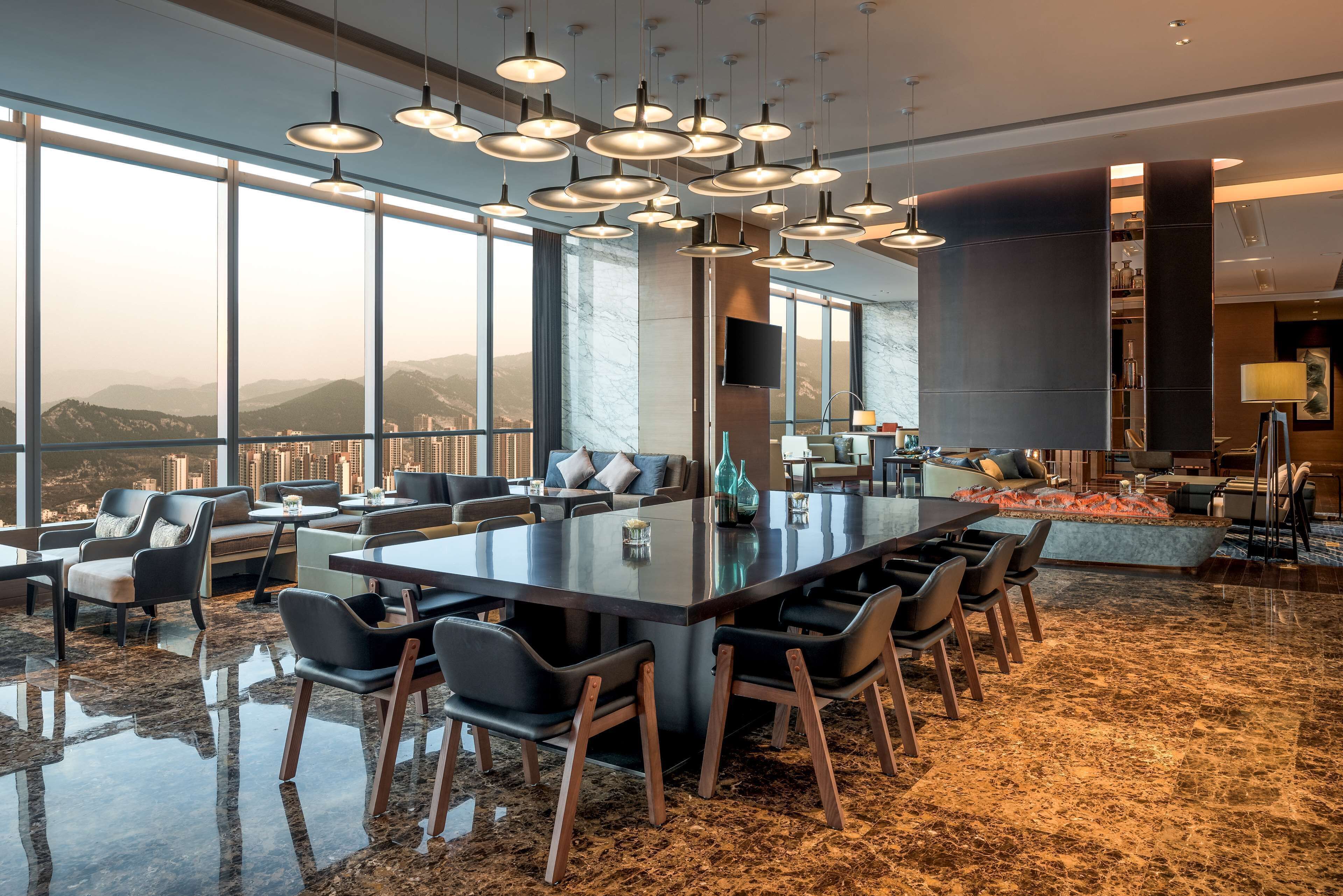 A spacious living area with a large central table, multiple seating options, and a city view through large windows.