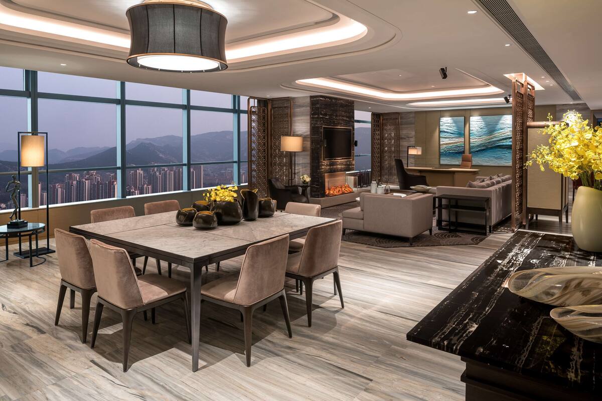 A modern living room with a large dining table, comfortable seating, a fireplace, and a city view through large windows.