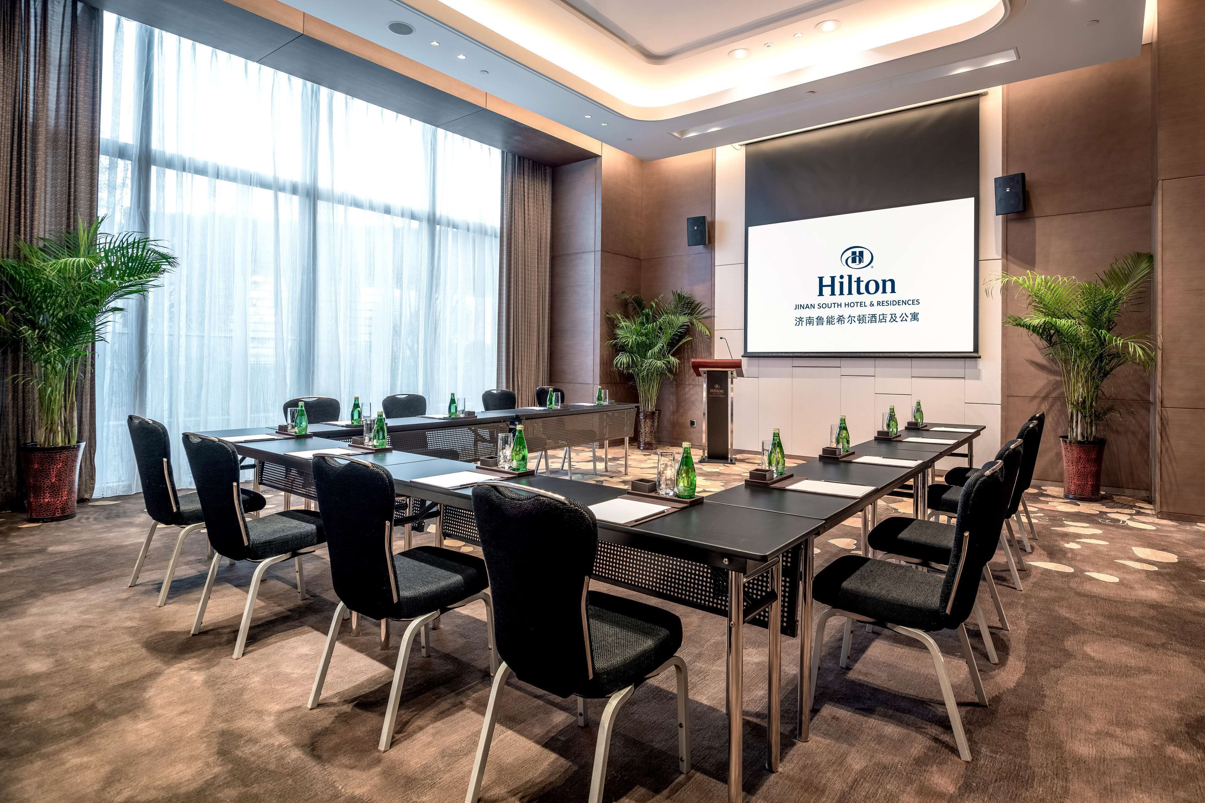 A conference room with a long table, black chairs, and potted plants.