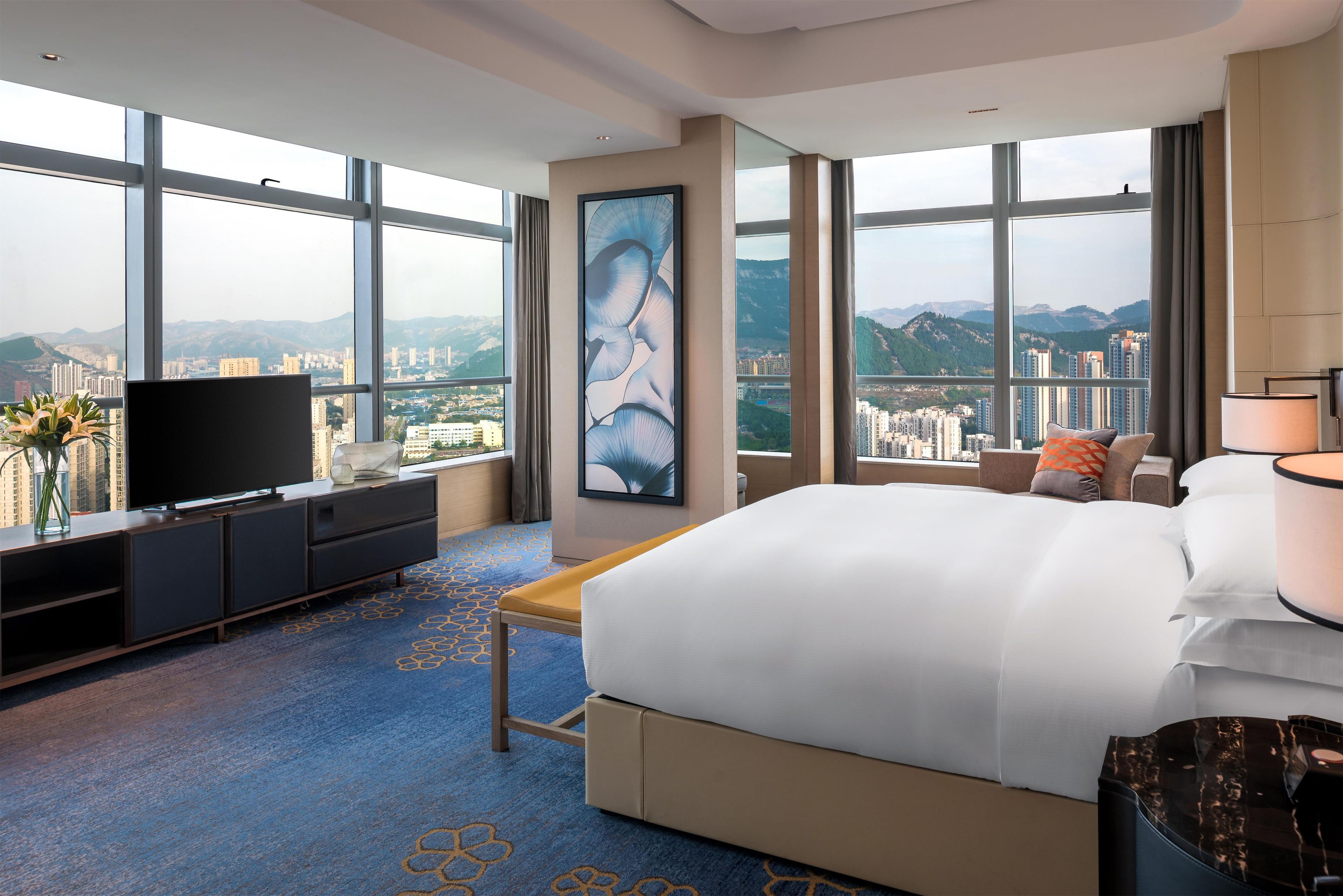 A hotel room with a large bed, a TV, a desk, and a view of a cityscape.