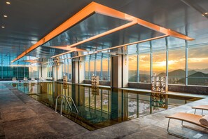 A modern indoor pool area with glass walls, a lounge with seating, and a view of the sunset through large windows. - Hilton Jinan South Hotel & Residences (Jinan)