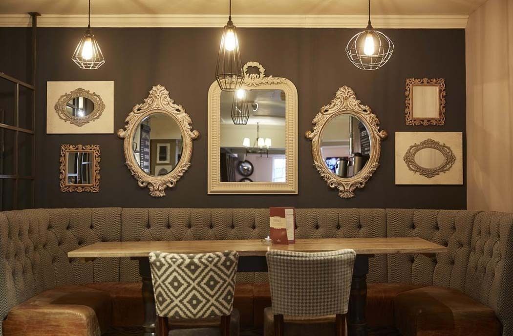 A dining area with a long wooden table, upholstered booth seating, and three ornate mirrors on the wall.