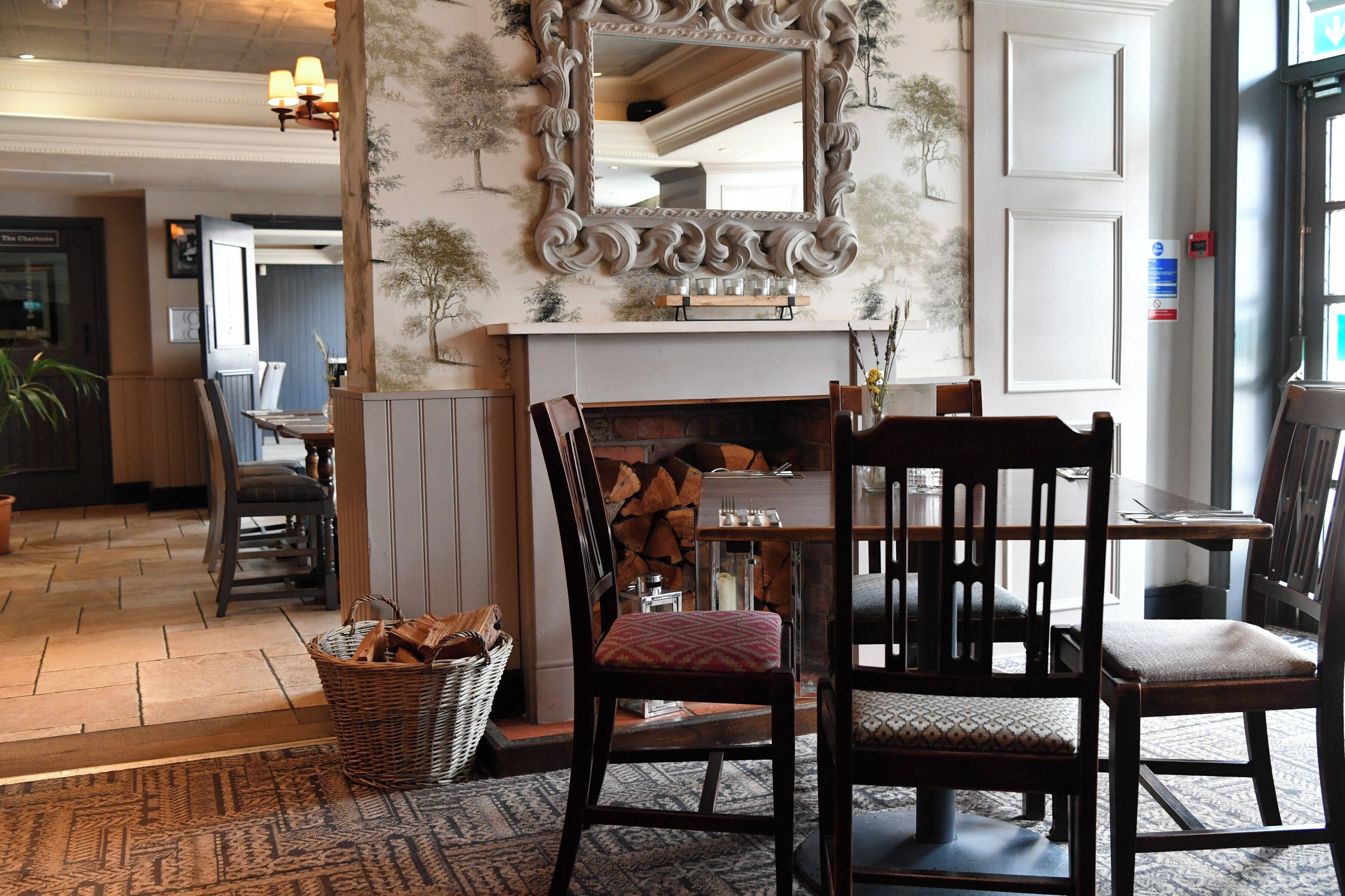 A dining area with a fireplace, wooden chairs, a table, and a mirror above it.