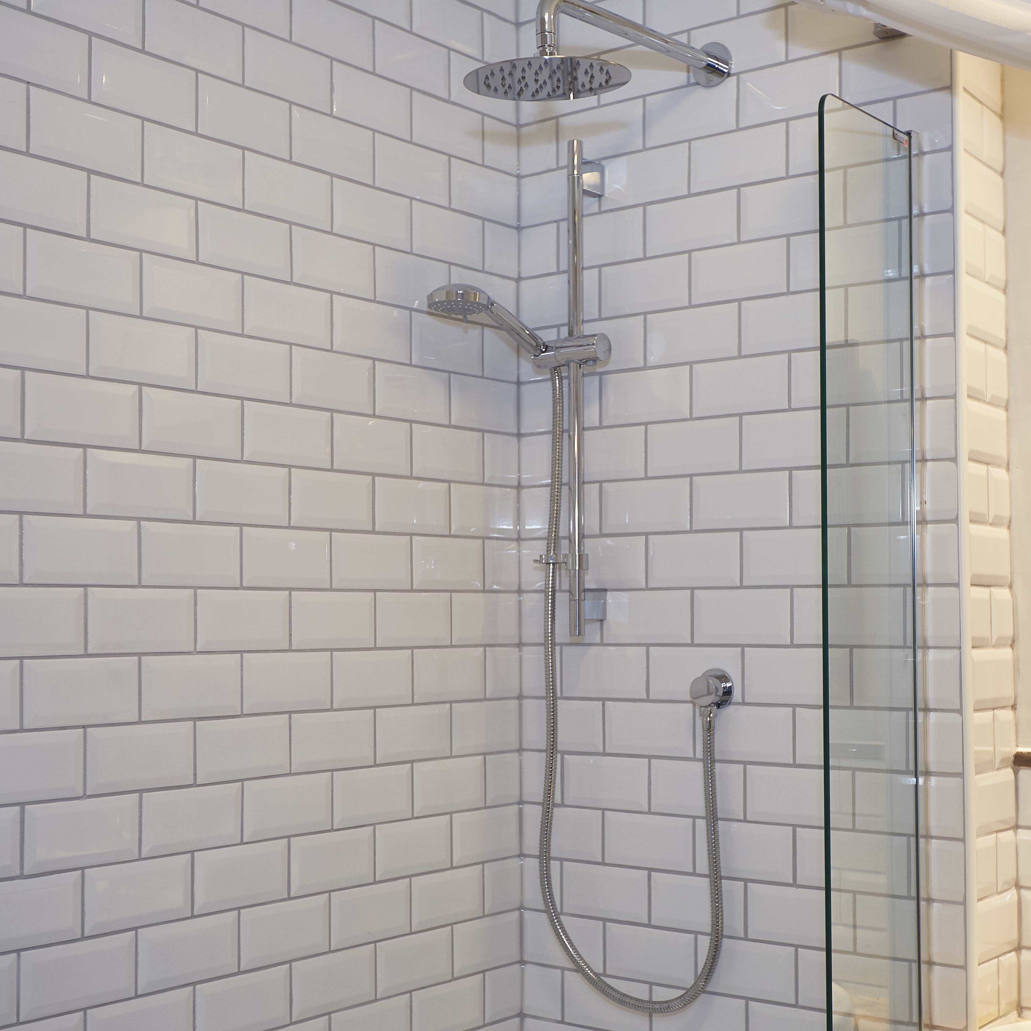 Una doccia con porta in vetro, accessori cromati e pareti rivestite di piastrelle bianche.
