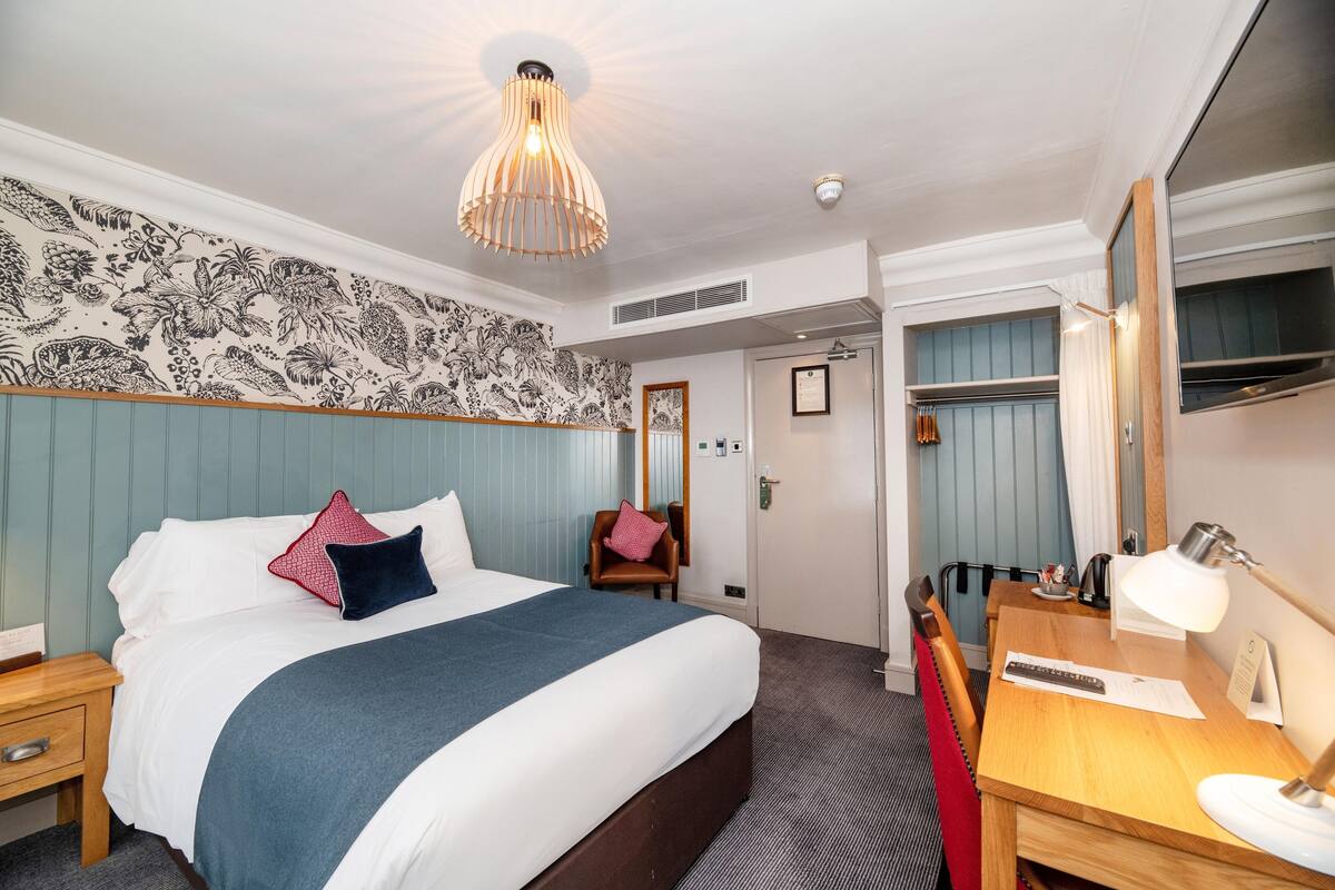 Hotellihuone, jossa on suuri sänky, työpöytä lampun kanssa, tuoli ja vaatekaappi.