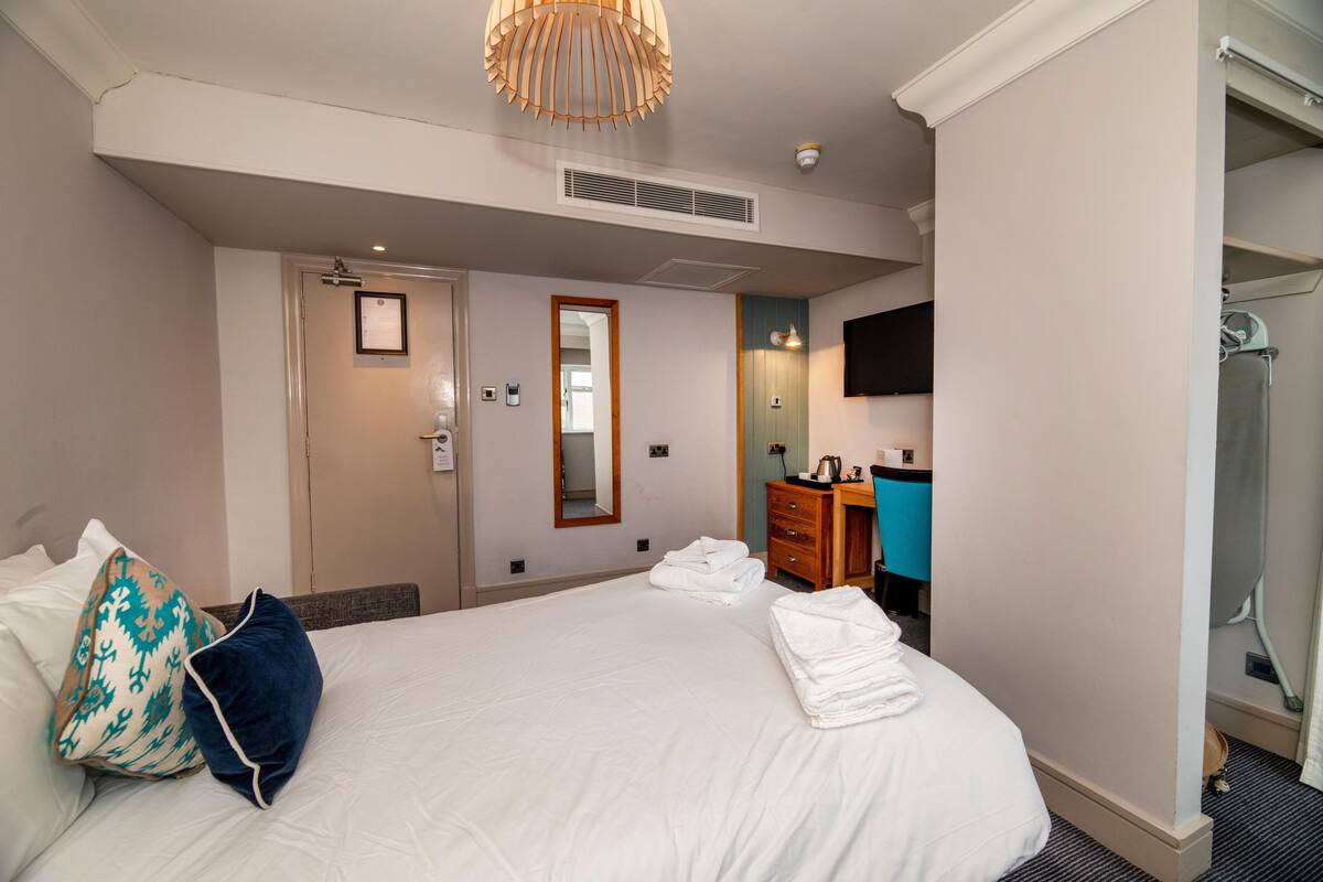 Hotellihuone, jossa on suuri sänky, puinen lipasto, peili ja suihkutila.