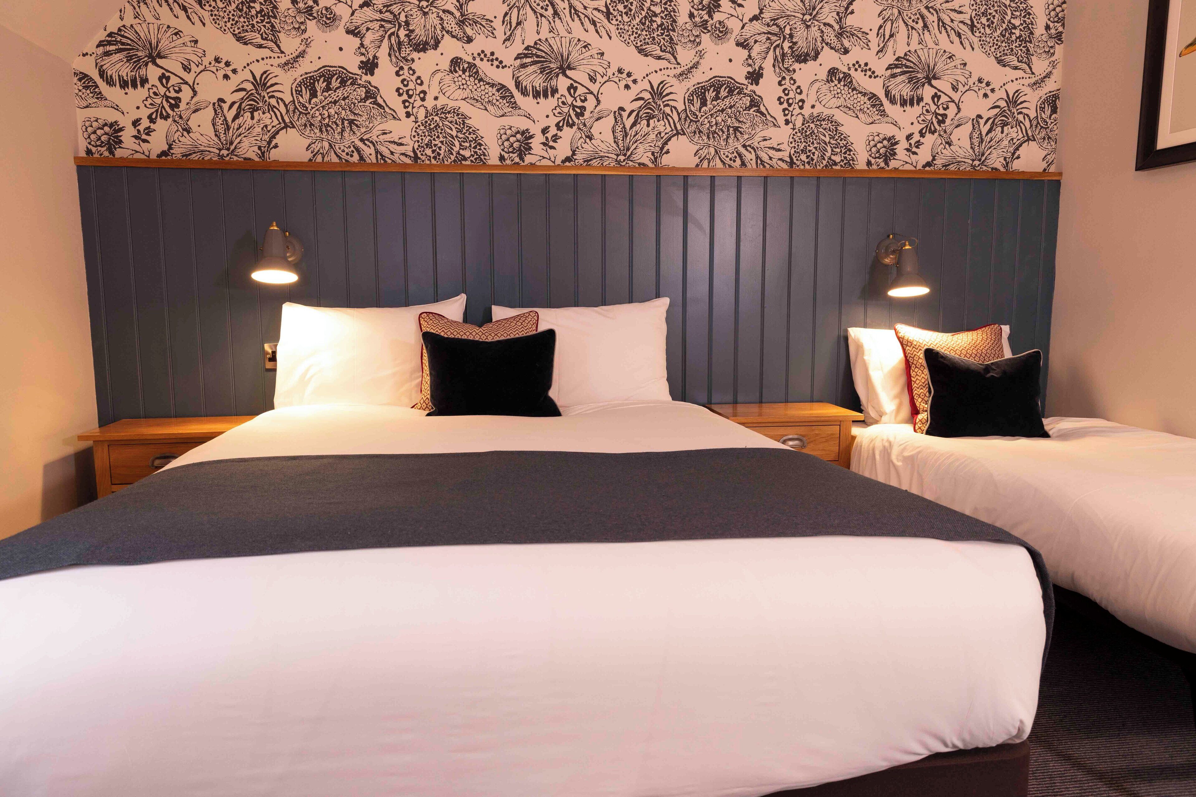 A double bed with a dark headboard, two bedside lamps, and a floral-patterned wallpaper.