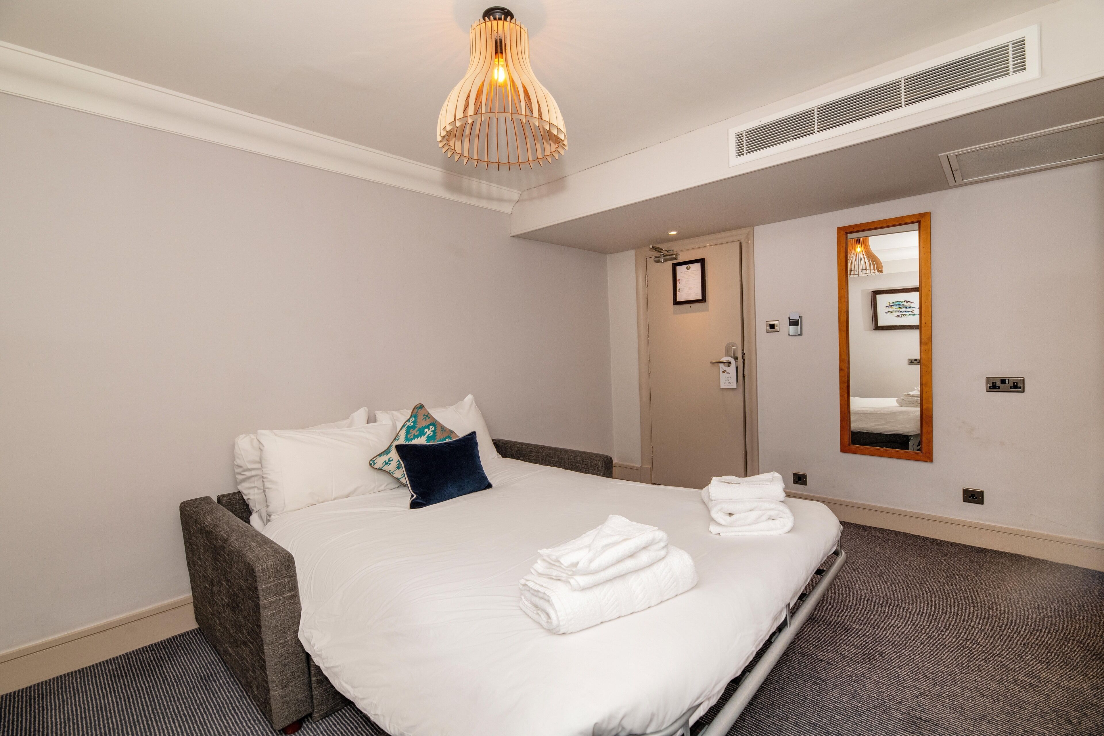 Une chambre d’hôtel comprenant un lit, une table de chevet, un miroir et un luminaire au plafond.