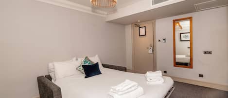Une chambre d’hôtel comprenant un lit, une table de chevet, un miroir et un luminaire au plafond.