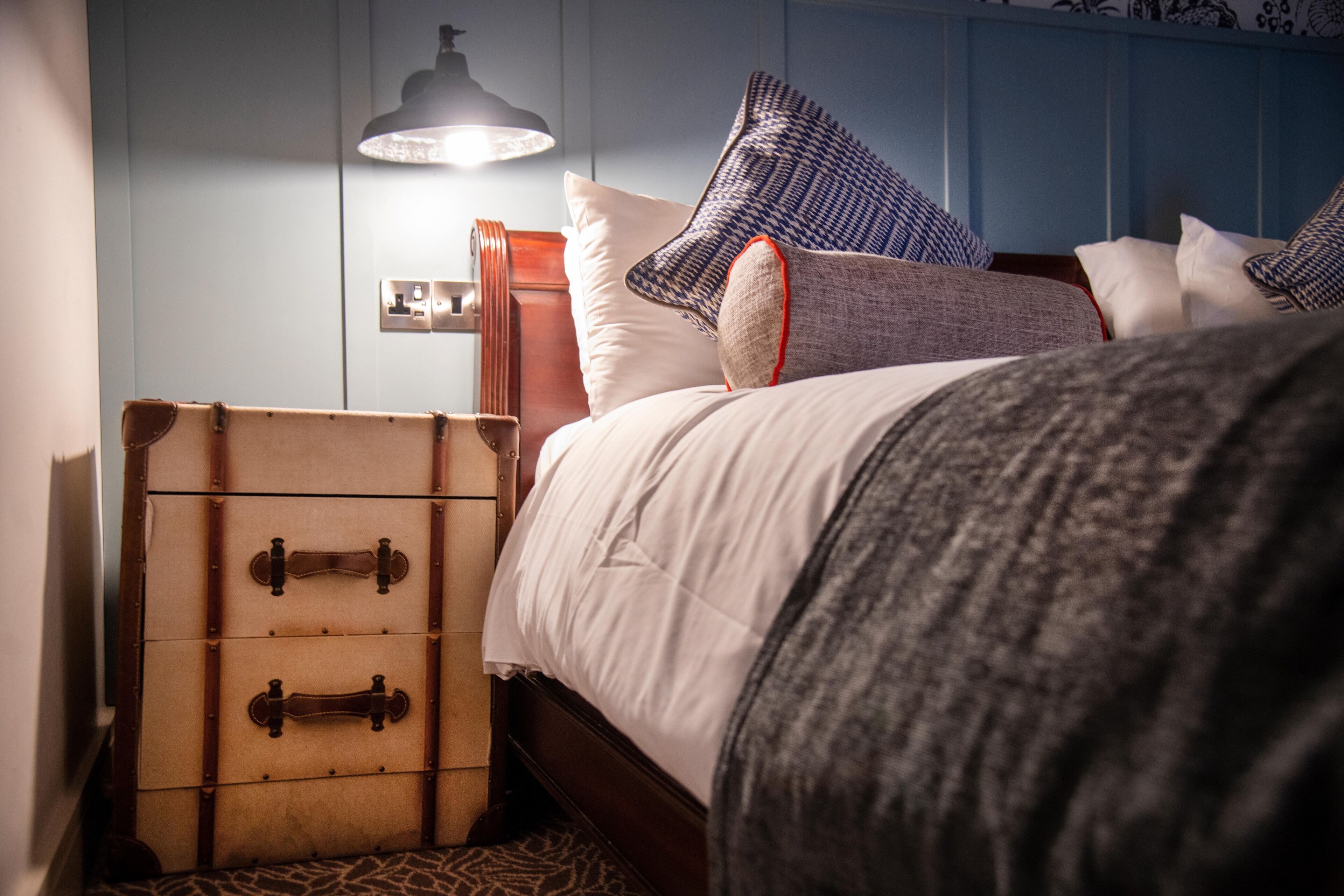 Una cama con una maleta y una lámpara en una habitación con pared azul y papel tapiz estampado.