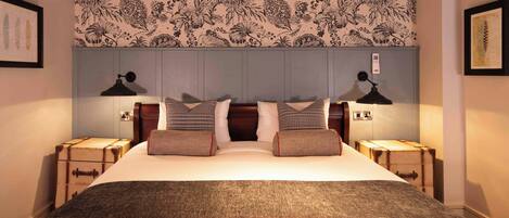 A neatly made bed with a grey blanket, two bedside tables with lamps, and a floral-patterned headboard.