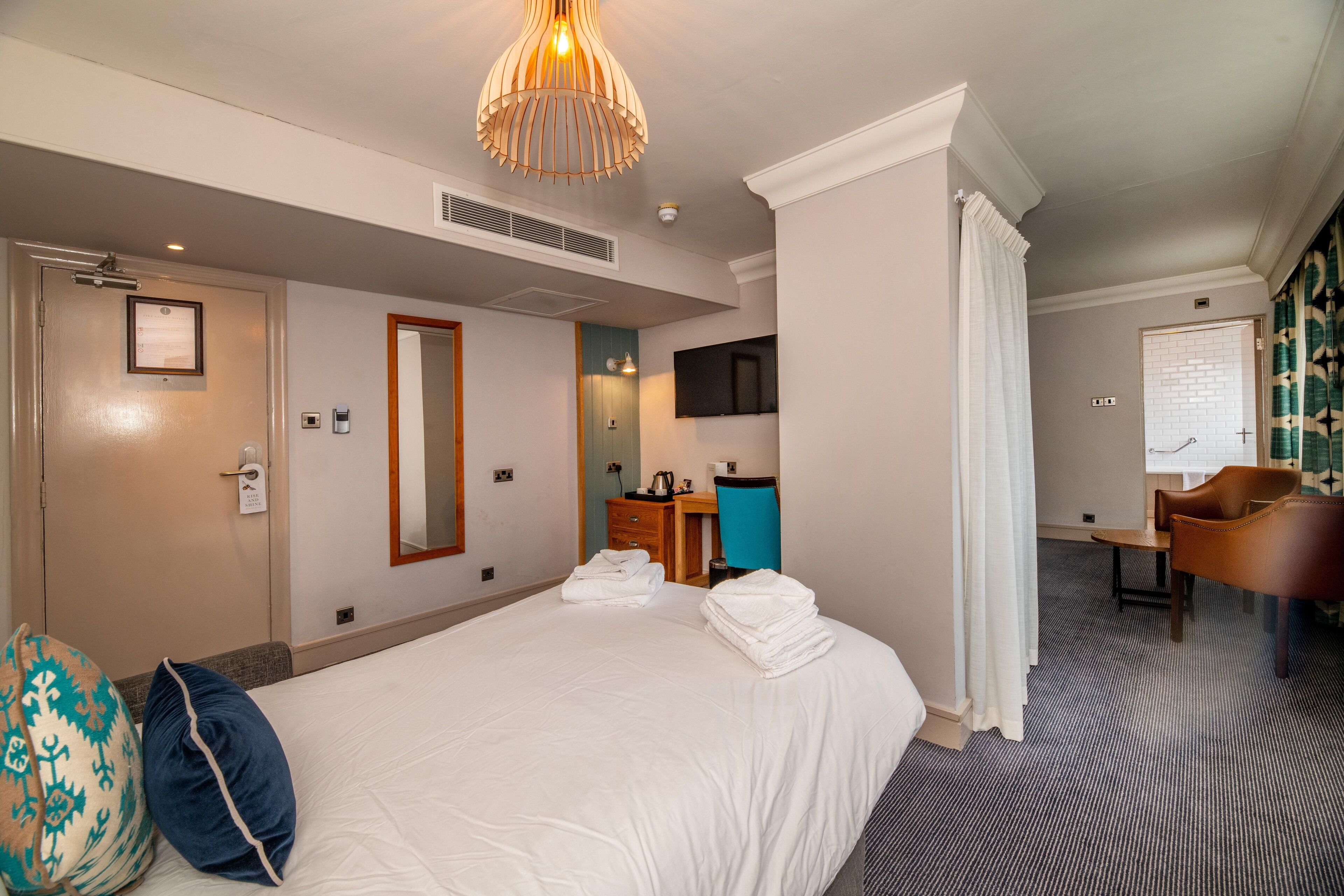 A hotel room with a large bed, a desk, a chair, a television, and a bathroom.
