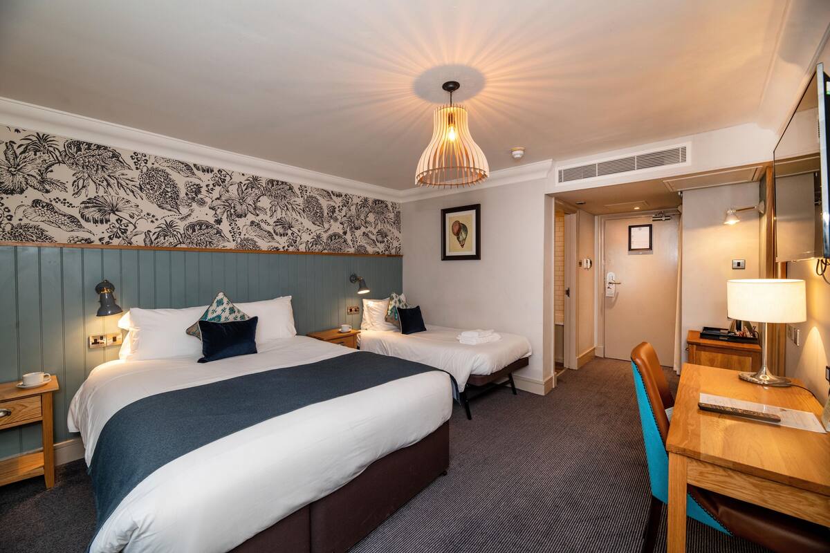 Hotellihuoneessa on kaksi sänkyä, työpöytä ja tuoli. Huoneessa on kattovalaisin, seinälle ripustettu taulu ja ovi, joka johtaa toiseen huoneeseen.
