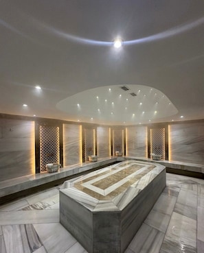 Ein moderner Wellnessbereich mit einem zentralen beheizten Pool, Marmorwänden und indirekter Beleuchtung.