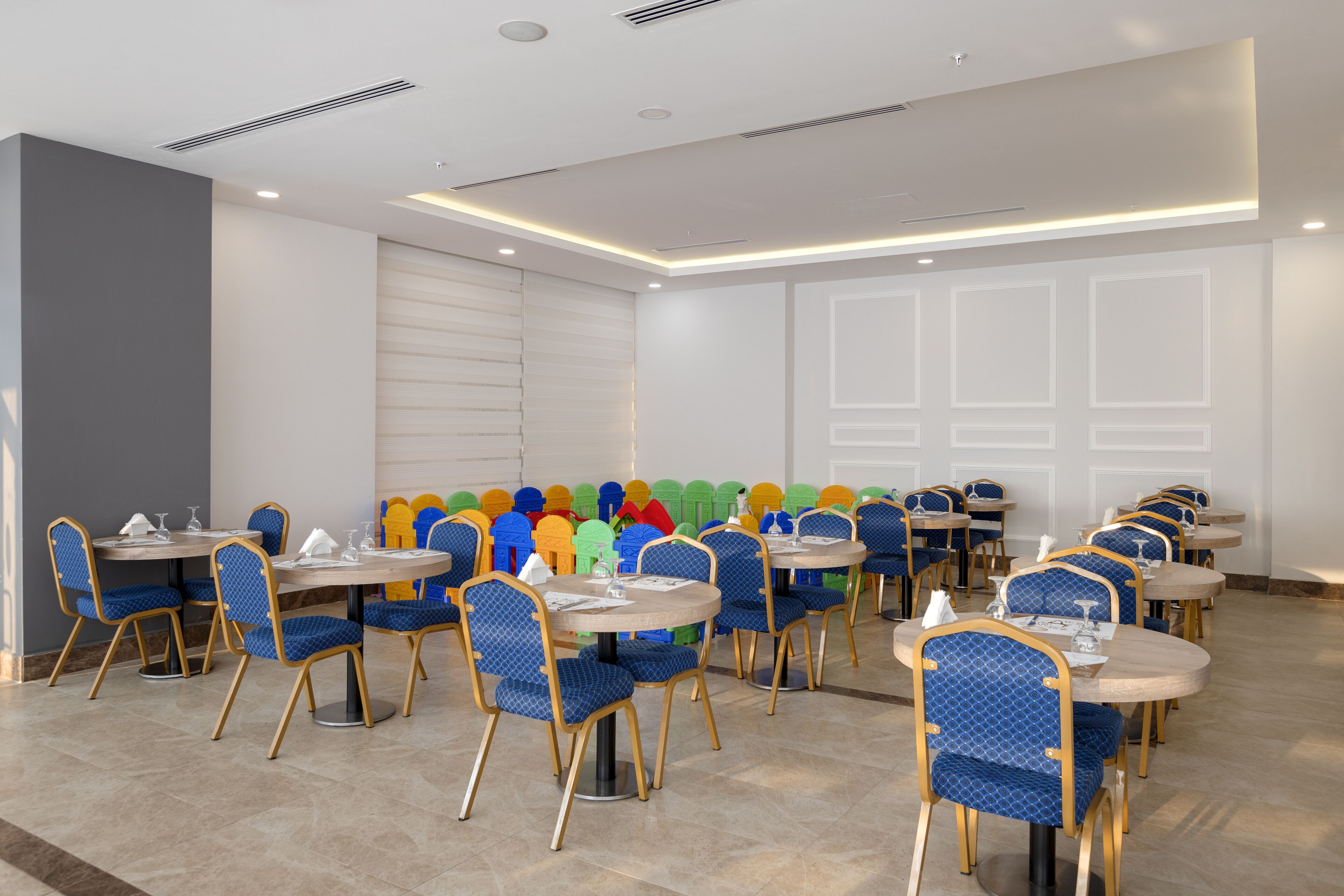 A dining area with round tables and blue chairs, featuring a modern design with recessed lighting and a tiled floor.