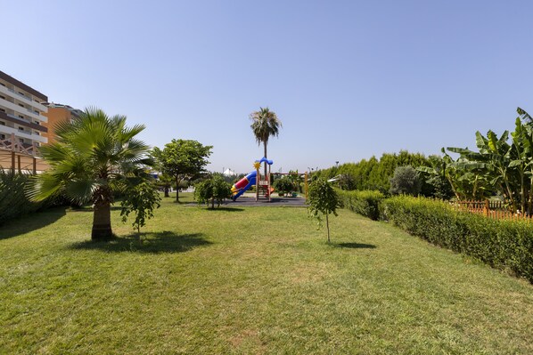 A park with a playground, palm trees, and a building in the background.