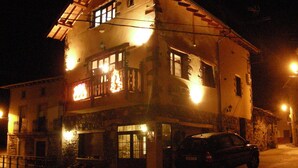 Un immeuble de deux étages avec un balcon à l’étage supérieur, une voiture garée devant et un lampadaire à proximité.