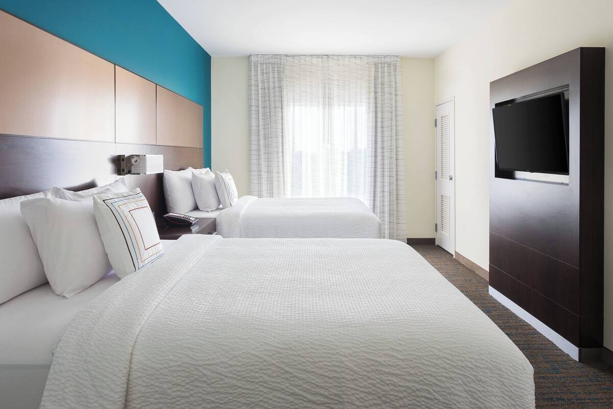 Una habitació d'hotel amb dos llits, una televisió, una taula de treball amb una làmpada i una finestra amb cortines.