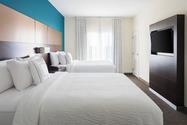 Habitación de hotel con dos camas, televisión, escritorio con lámpara y ventana con cortinas.