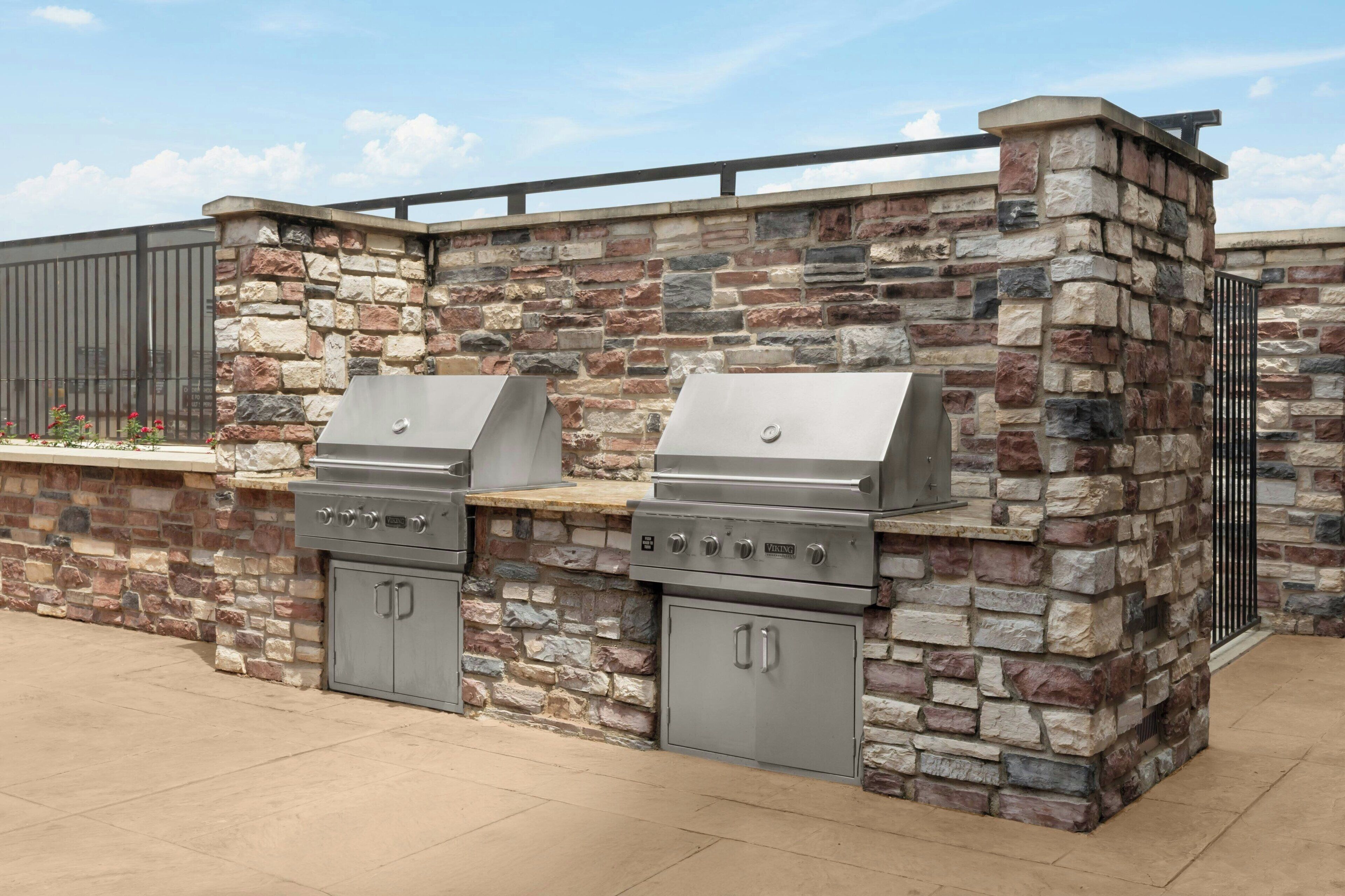 A stone-built outdoor kitchen with two stainless steel grills and a built-in sink.