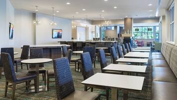 En hotellobby med flere siddeområder, herunder borde og stole, en receptionsdisk og et stort vindue med udsigt udendørs.