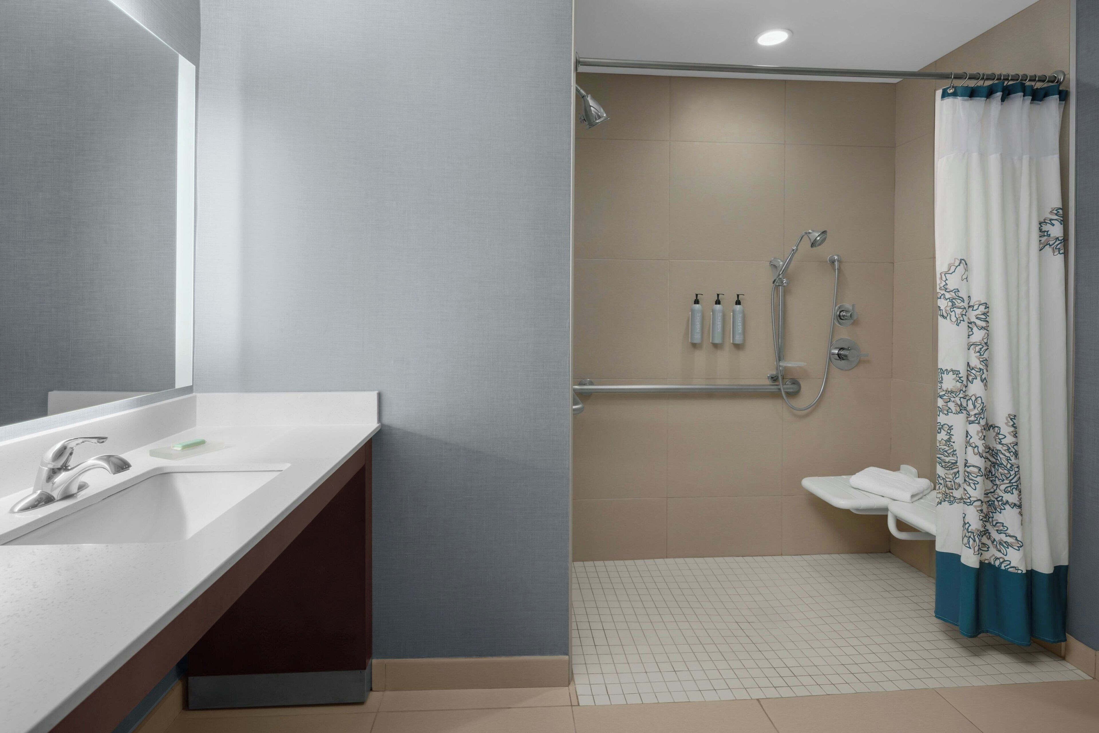 Un baño moderno con lavamanos, espejo, ducha e inodoro.