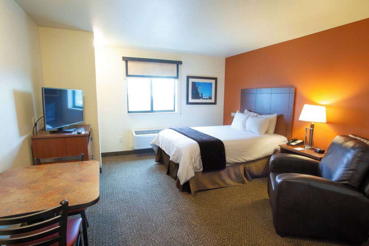 Ein Hotelzimmer mit einem Bett, einem Schreibtisch mit Fernseher, einem Sessel und einer Lampe.