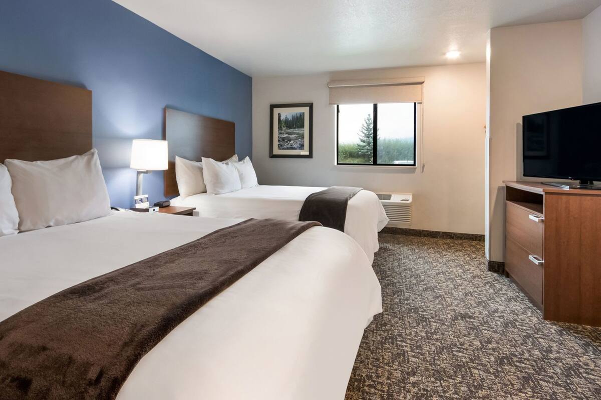 Ein Hotelzimmer mit zwei Betten, einem Fernseher, einem Schreibtisch, einem Fenster und einem Bild an der Wand.
