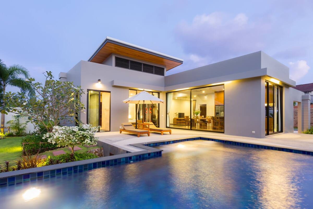 Une maison moderne dotée d’une piscine, de grandes fenêtres et d’un espace patio.
