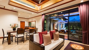 A modern living area with a sofa, dining table, chairs, and a large window with curtains. - Nai Harn Baan-Bua Villas (Rawai)