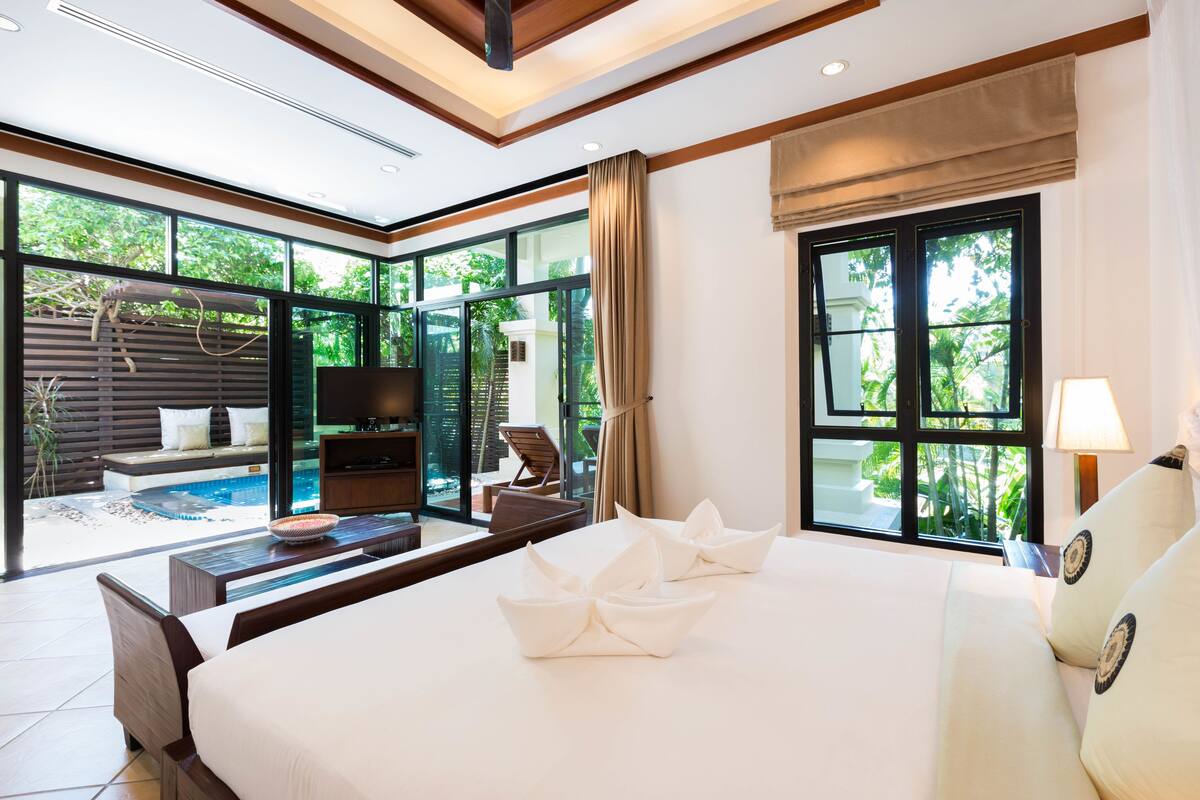 Une chambre d’hôtel moderne dotée d’un grand lit, d’une télévision, d’un bureau et offrant une vue sur une piscine et un espace de détente extérieur.