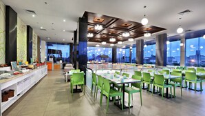 Un comedor moderno con sillas y mesas verdes, ventanas amplias y vistas a la ciudad.