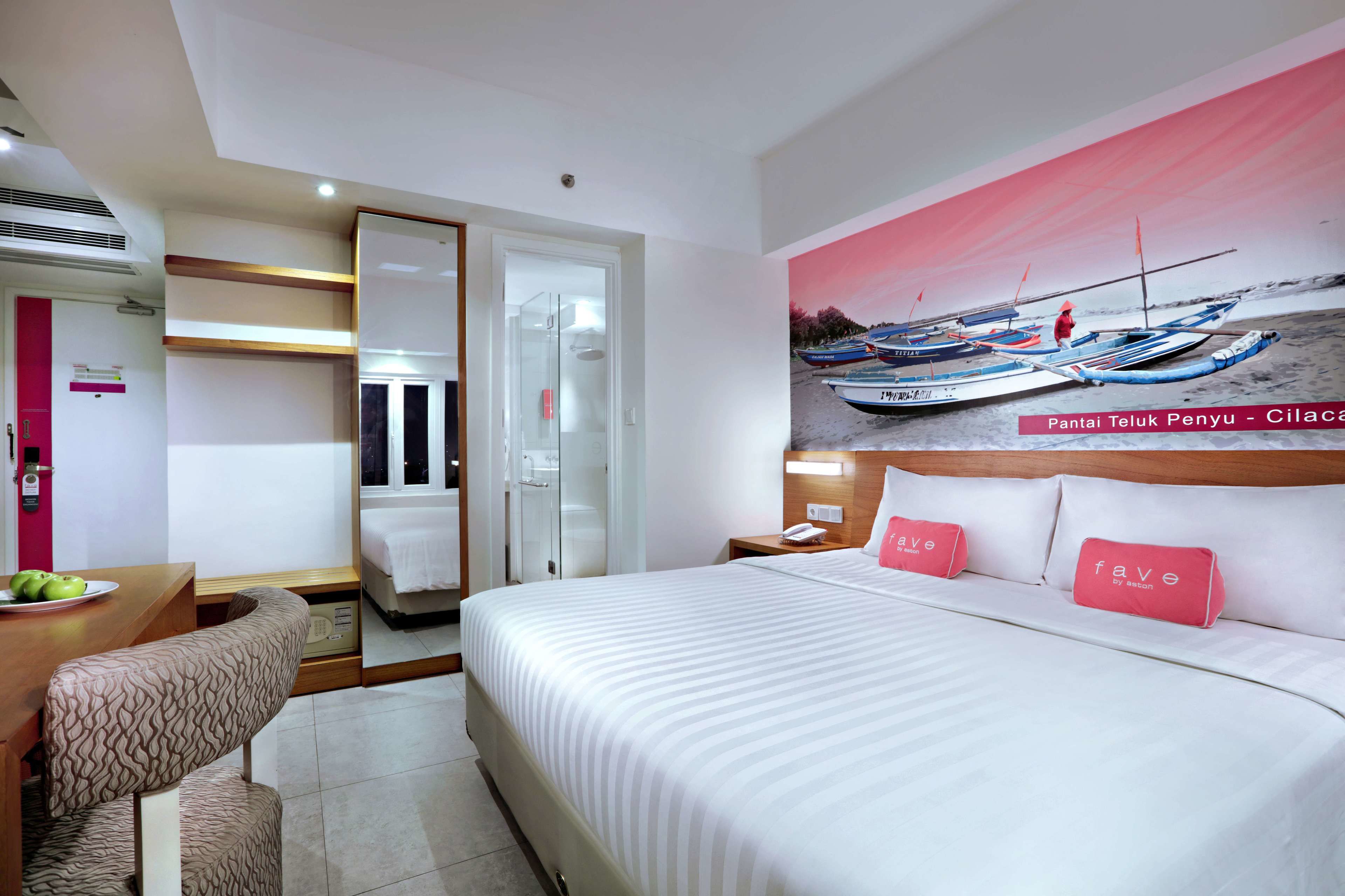 A modern hotel room with a large bed, a desk with a chair, a wardrobe, and a bathroom.