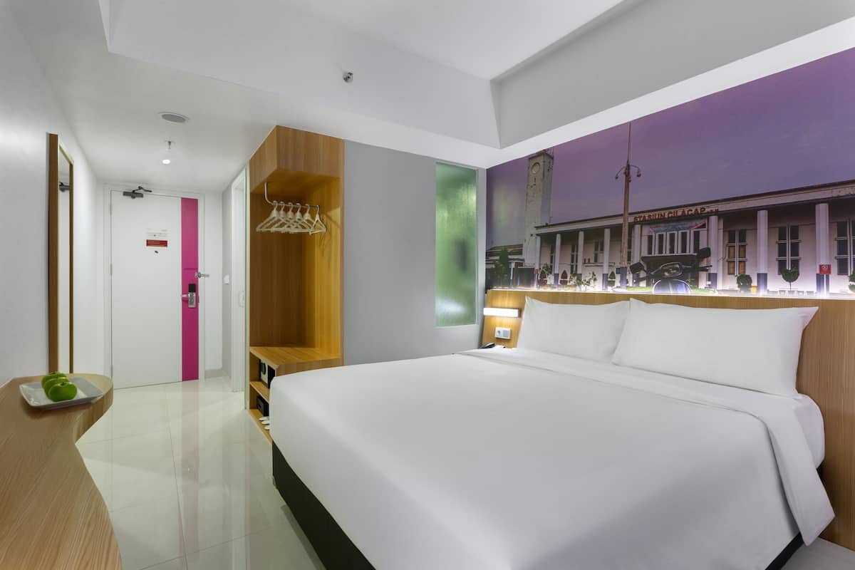 A modern hotel room with a large bed, a wooden wardrobe, a seating area, and a wall mural.