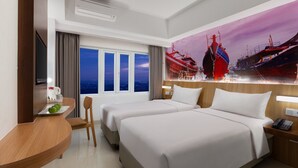 Habitación de hotel con dos camas, un escritorio con silla, un televisor y un ventanal con vistas a barcos.
