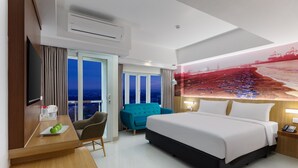 Una habitación de hotel moderna con una cama grande, un escritorio con silla, un sofá y un ventanal con vistas a la ciudad.