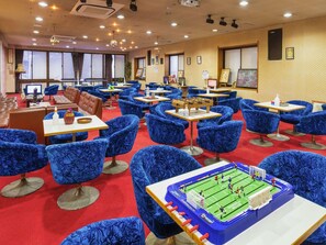 Un hall d’hôtel avec des fauteuils, des tables et un baby-foot, le tout recouvert d’un tissu bleu.