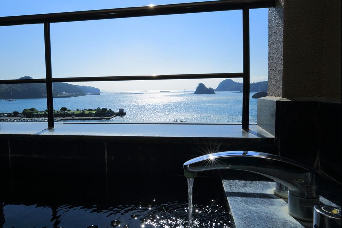 A window with a view of a calm body of water, a distant landmass, and a clear sky.