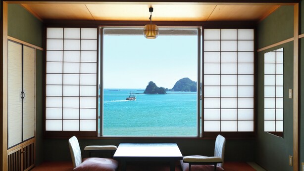 Ein traditioneller Raum mit Tatami-Boden, einem niedrigen Tisch, zwei Kissen und Blick aufs Meer durch Shoji-Schirme.