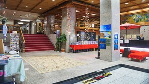 Eine Hotelhalle mit einer zentralen Treppe, einem Empfangsbereich und einer Zeitschriftenauslage.